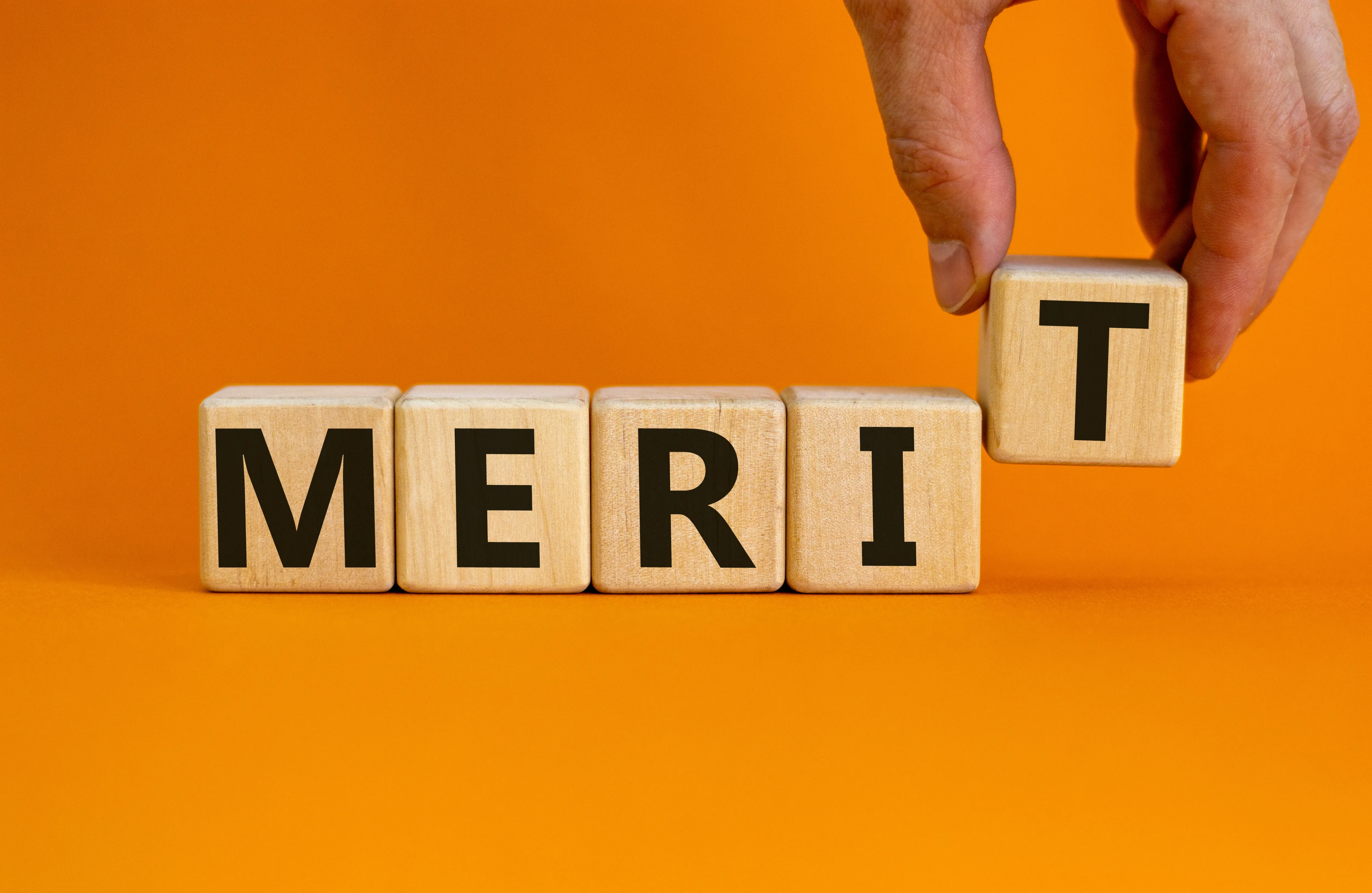 「MERIT」と書かれたブロックを並べる手元のイメージ。
