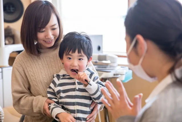 お母さんの膝の上で歯磨きをする男の子の画像
